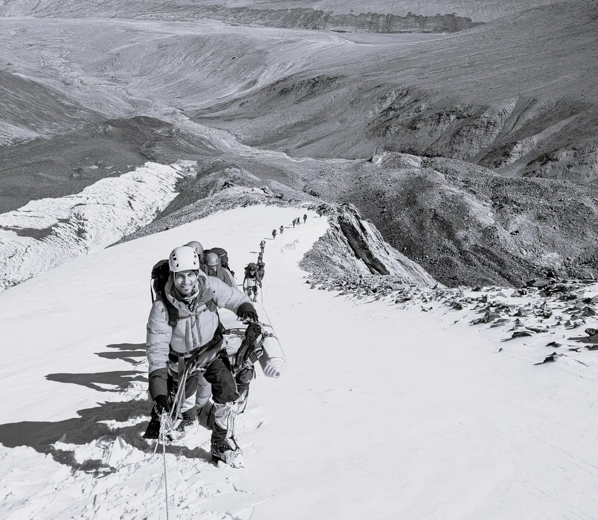 A lead climber heading a roped party up a snow slope, a mountain range behind